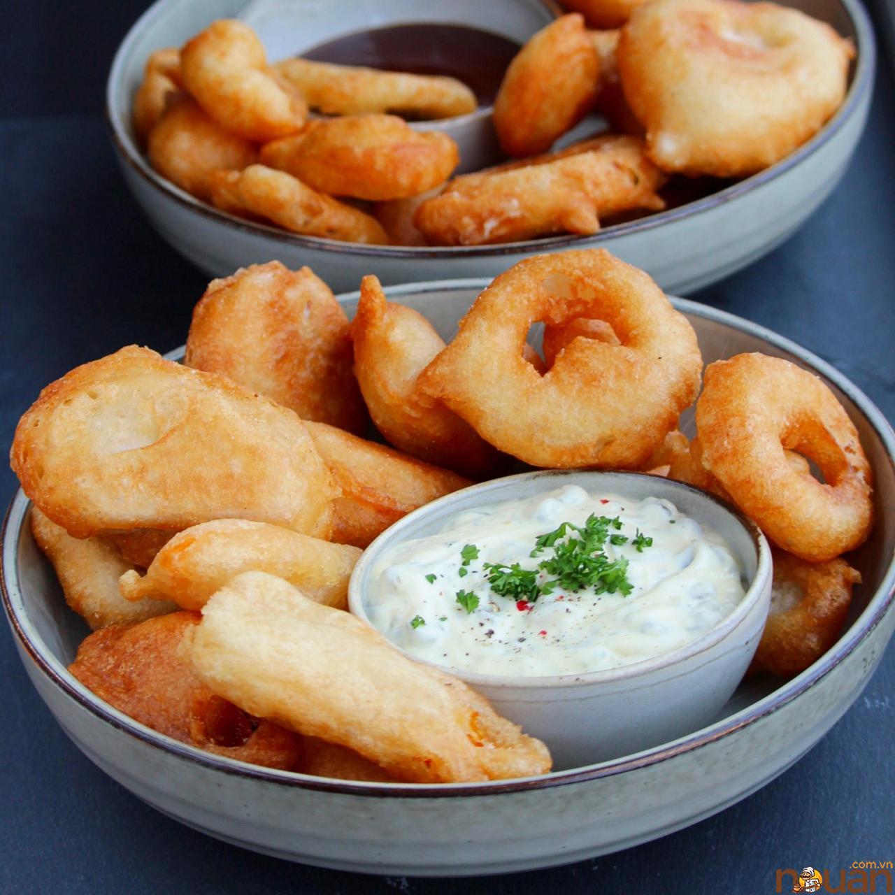 a bowl of crispy-looking beer-battered chicken and onion rings surrounding a ramekin of tartar sauce garnished with chopped parsley